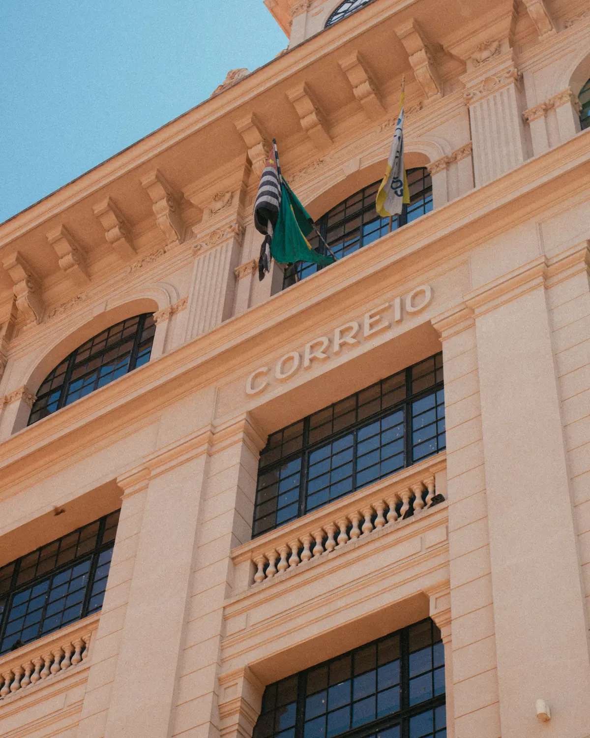 Fachada de edifício público histórico em São Paulo, com as bandeiras do Brasil e do Estado